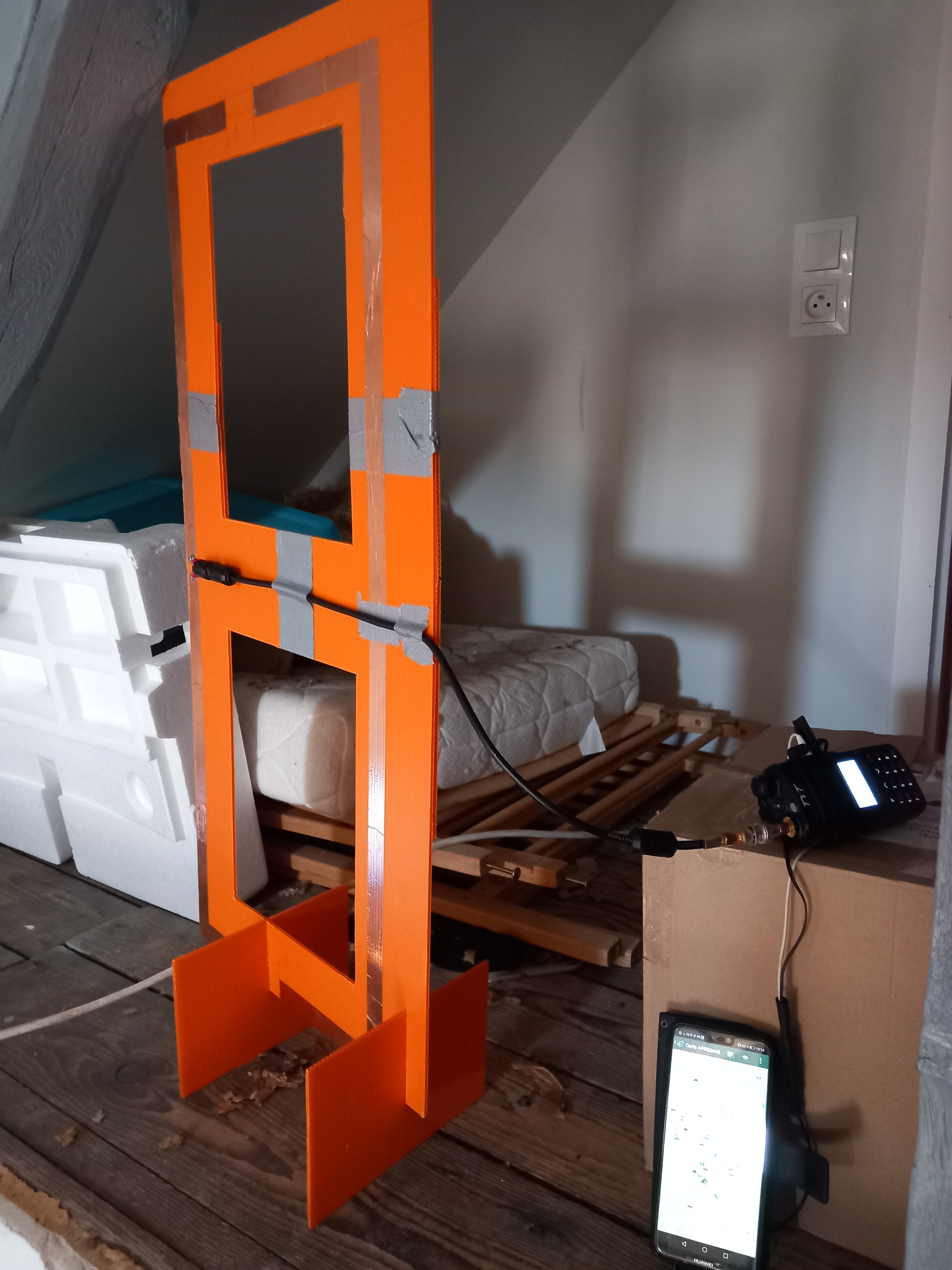 Moxon antenna made of copper tape on an orange plastic board. Other pieces of tapes keep the coaxial straight. Two other plastic pieces are used to keep it stand up.